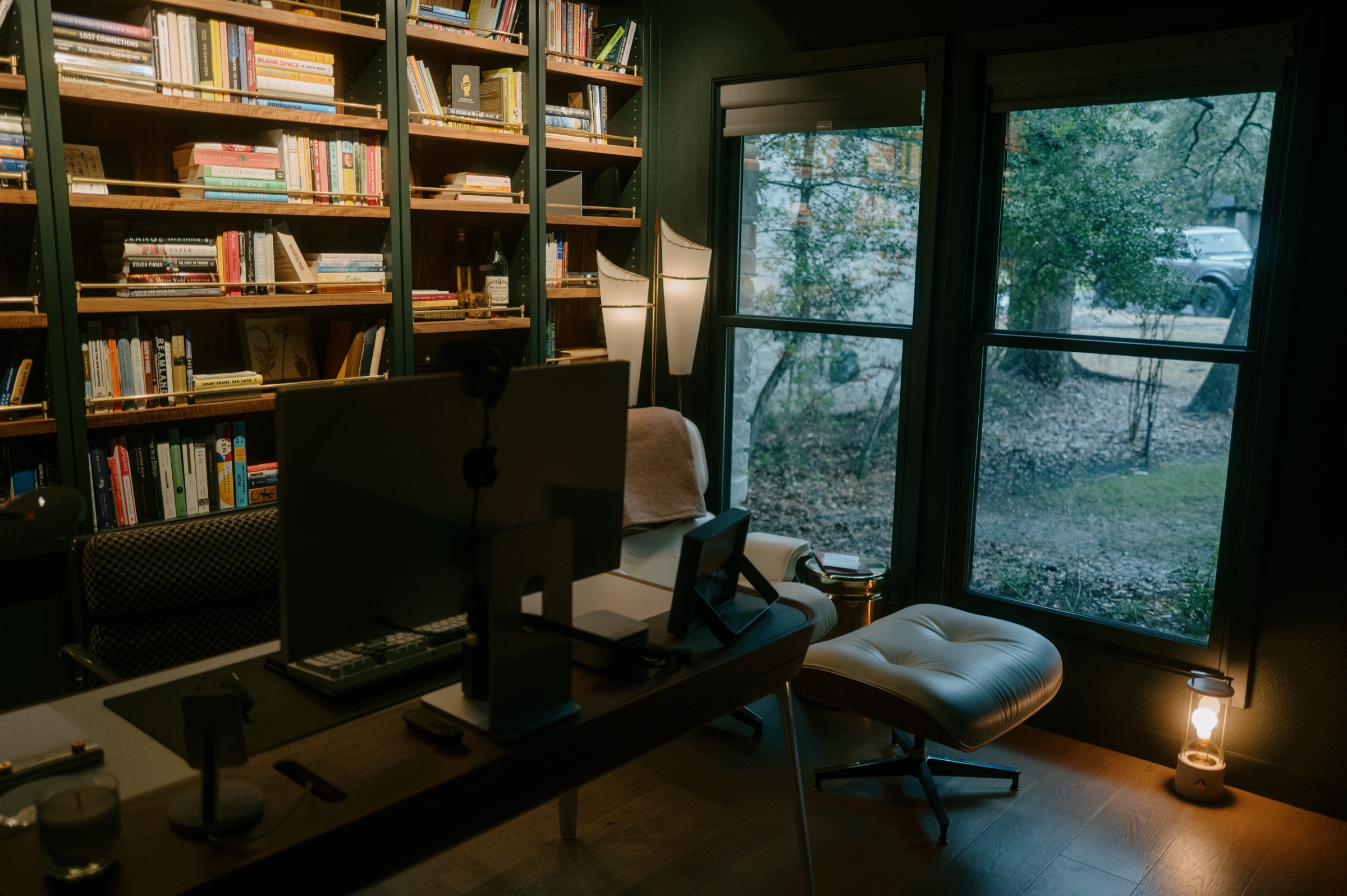 My office: walnut bookshelves, a white lounge chair, and windows onto the trees